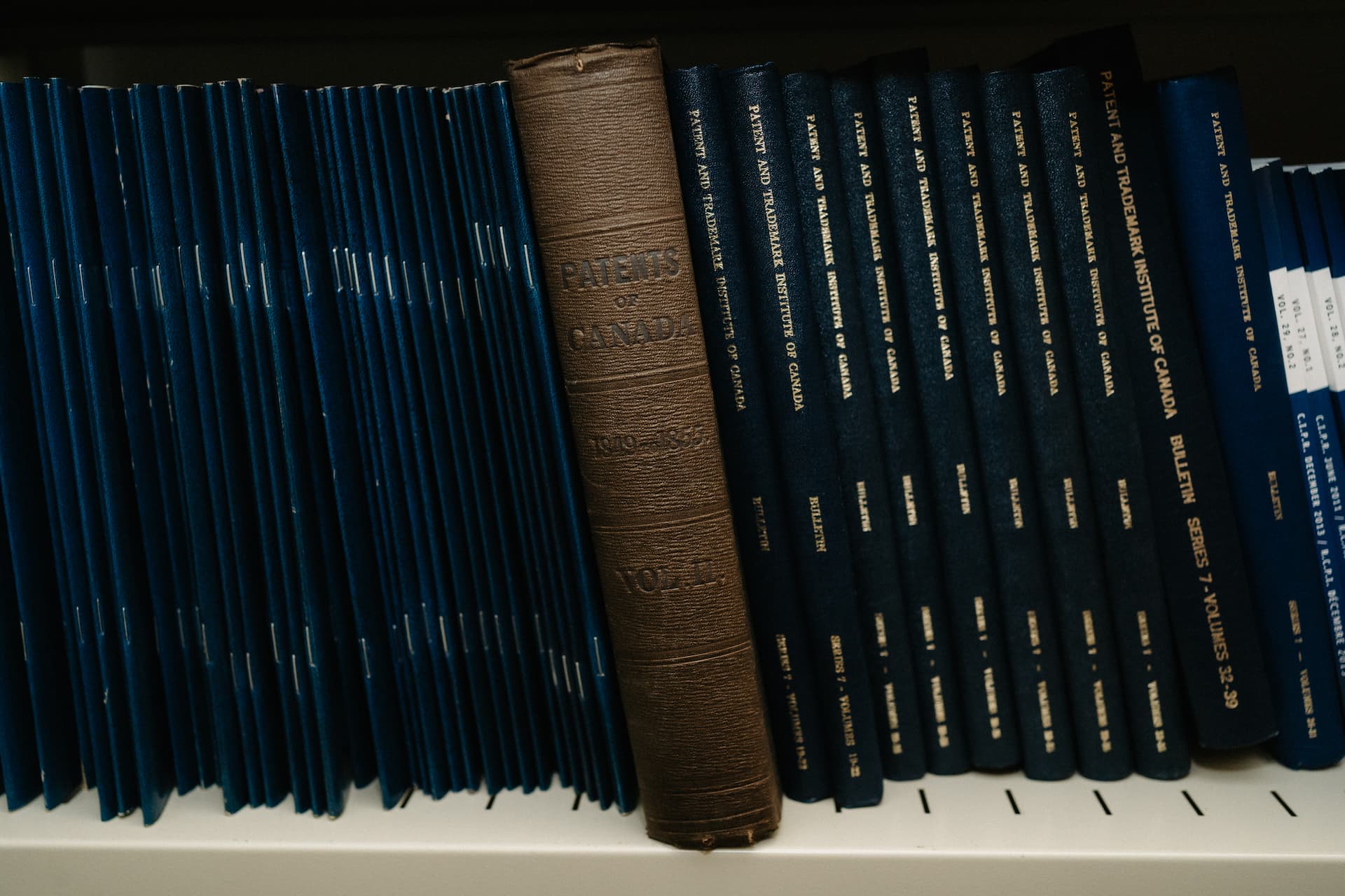 Un vieux livre relié en cuir intitulé « Patents of Canada » (Brevets du Canada) sur une étagère, parmi plusieurs volumes plus récents.