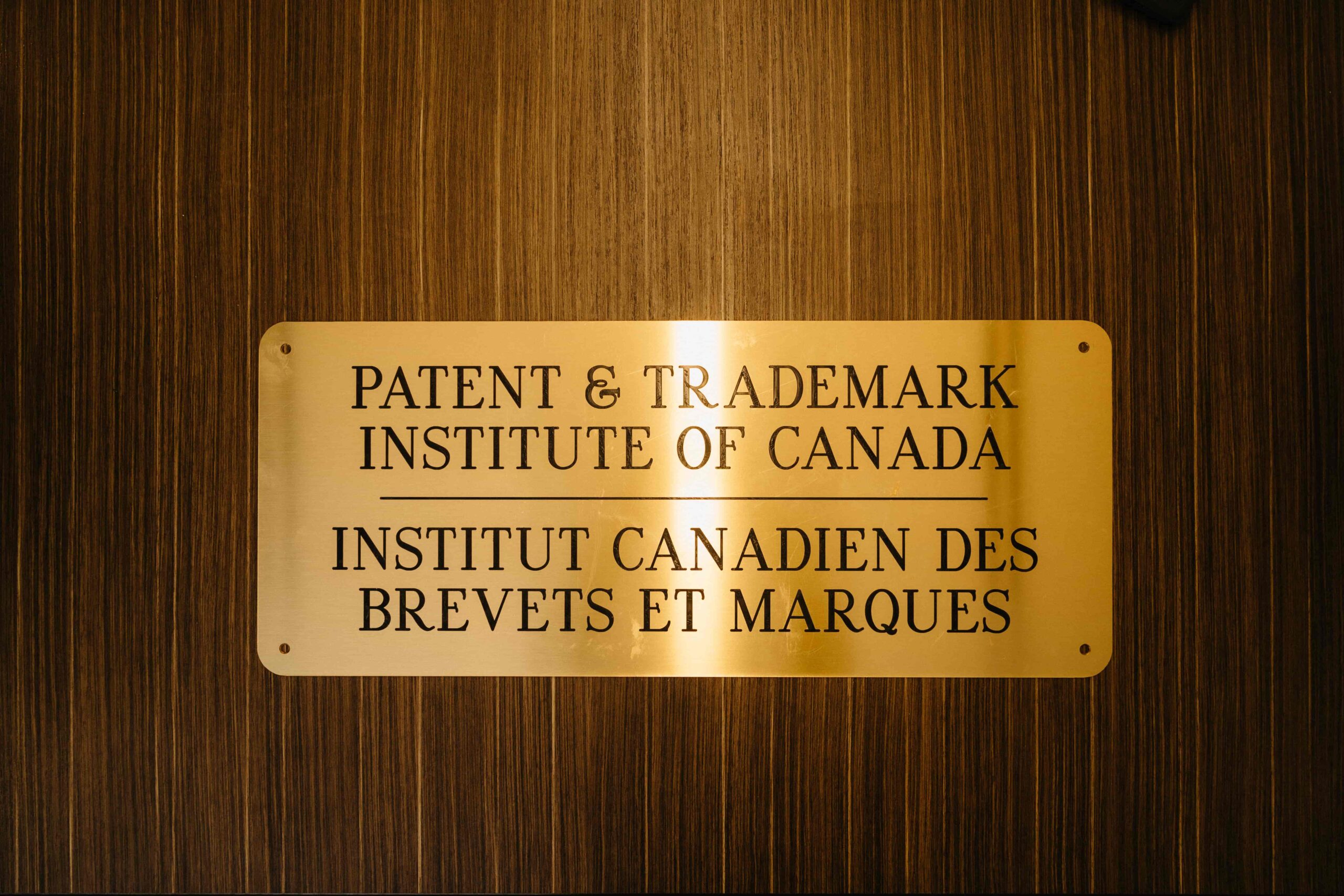 Une plaque dorée fixée sur un fond en bois porte l'inscription « Patent &amp; Trademark Institute of Canada | Institut Canadien des Brevets et Marques ».
